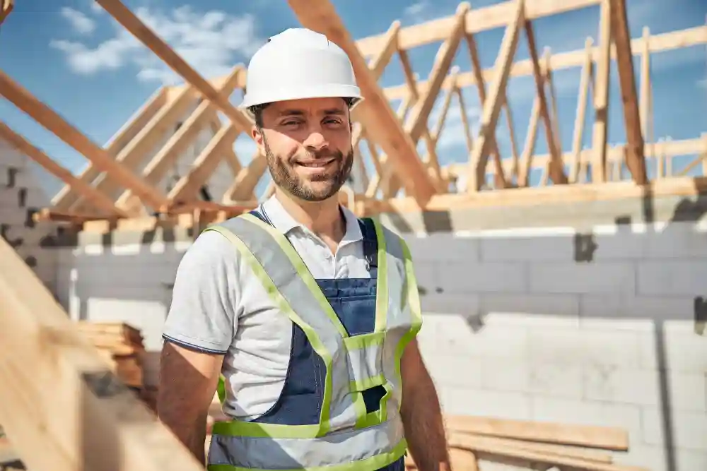 A smiling builder from G&M Building Contractors. He is on site standing in the sun near a roof that is being constructed in Oxfordshire or Berkshire.