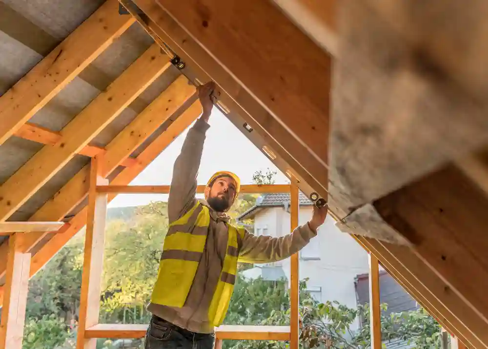 A G&M Builder is roofing a new building project near Oxford or Newbury in Oxfordshire and Berkshire. The image shows him reaching up and fitting some element of the beams together.