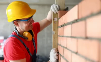 A tradesperson from G&M Building Contractors is brick laying on a building site in the sun.